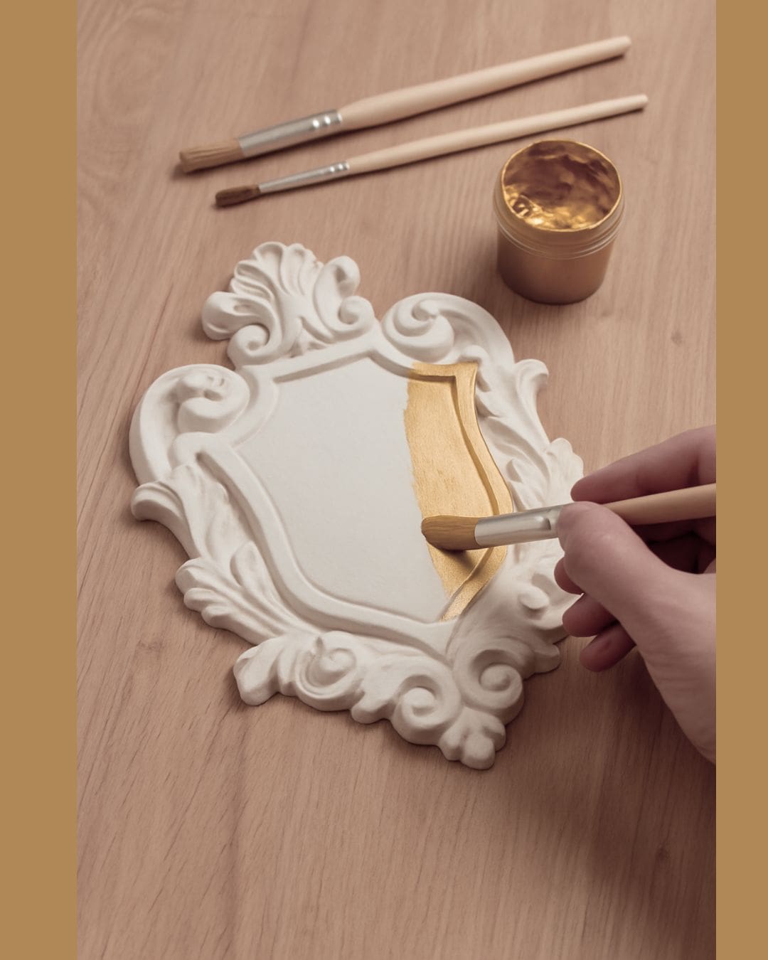 Proceso de pintura artesanal de un escudo de escayola con pincel y acabado dorado